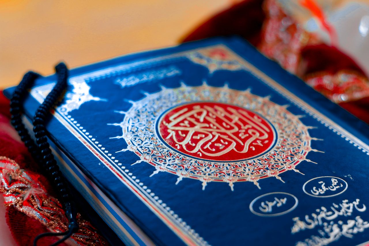 A close-up photograph of the Holy Quran with prayer beads, depicting Islamic spirituality.