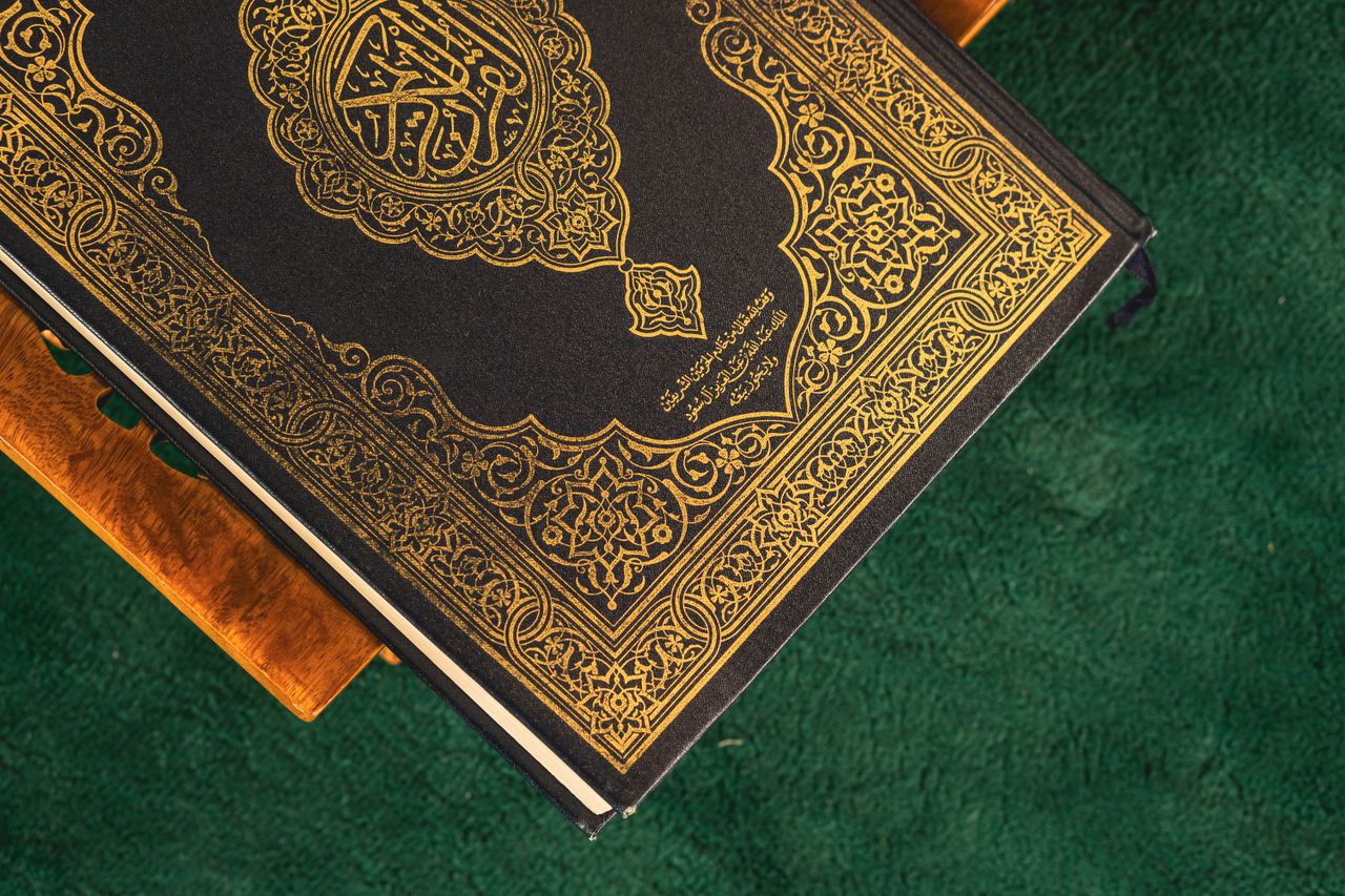 A Quran with an ornate golden design resting on a wooden stand against a green background.