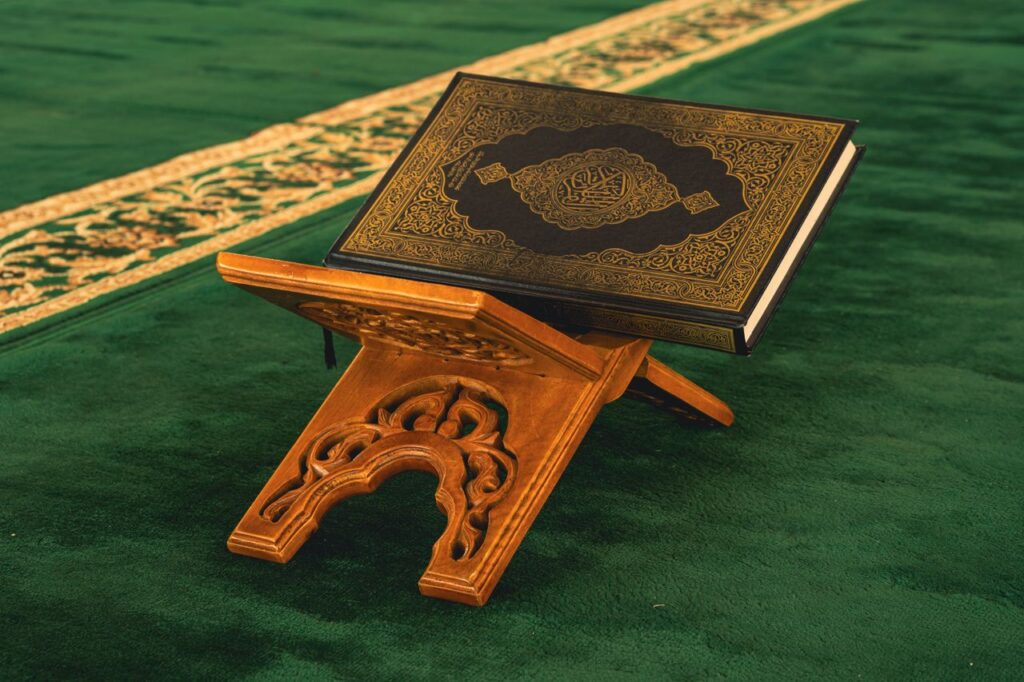 A beautifully ornate Quran placed on a traditional wooden stand in a mosque setting.
