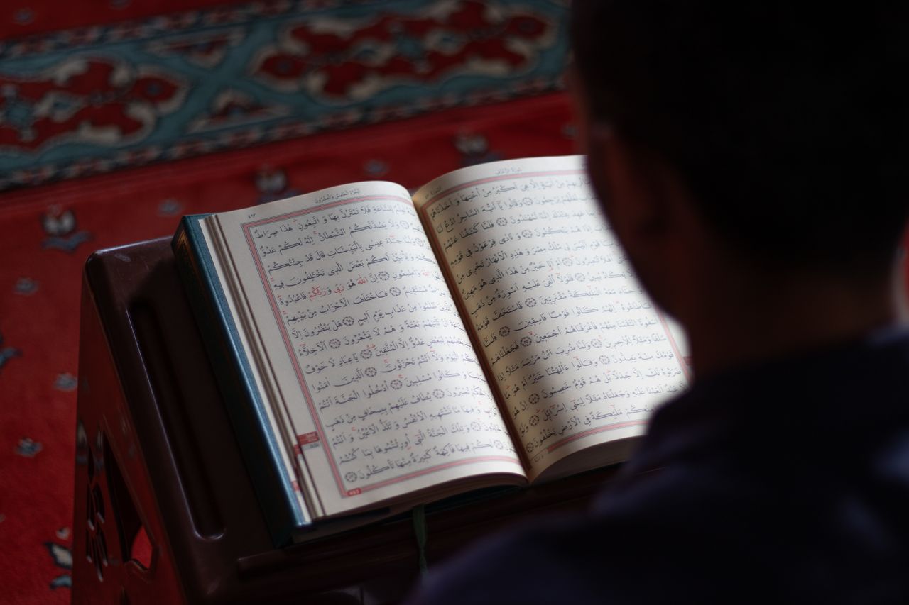 A person reads the Quran inside a mosque with intricate carpet design, reflecting peace and spirituality.