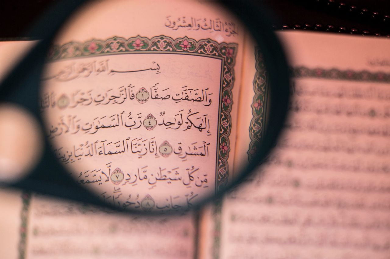 A detailed view of Arabic text in the Quran, highlighted by a magnifying glass, focusing on Islamic teachings.