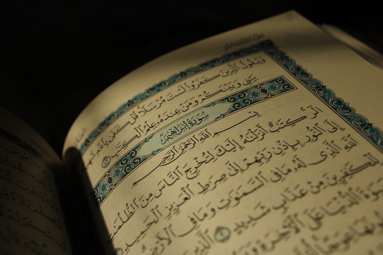 Close-up of an open Quran displaying Arabic calligraphy under warm lighting, conveying spirituality.